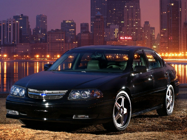 a 2004 chevrolet impala parked next to a cityscape and river at night